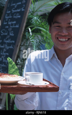 Didascalia: Luang Prabang, Laos - Sep 2003. Un cameriere serve caffè e torta presso un cafe in Luang Prabang. Poco più di una città fantasma di dieci anni fa, Foto Stock