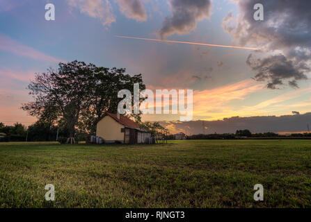 Casa isoloated nel campo al tramonto con il cielo nuvoloso Foto Stock