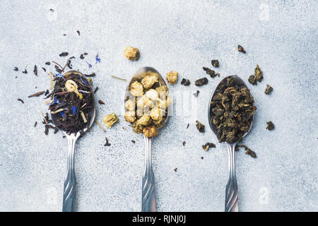 Varietà di tè a secco di foglie e fiori in cucchiai su sfondo grigio. Foto Stock