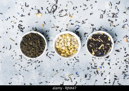 Varietà di tè a secco le foglie e i fiori in vaso su sfondo grigio Foto Stock