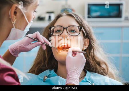 Bella donna dentista nella maschera esamina un paziente nello studio dentistico Foto Stock