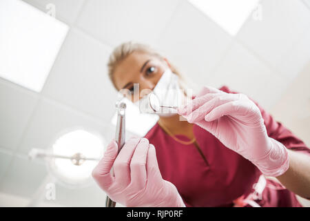 Bella donna dentista in maschera con i suoi strumenti. Vista dal basso Foto Stock