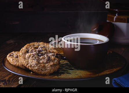 Farina di avena raisin cookie del dado e la tazza di caffè su una piastra vintage contro un oscuro sfondo di legno Foto Stock