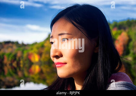 Una bella donna cinese guardando la luce del sole di mattina in autunno a Burr Pond State Park di Torrington, Connecticut. Foto Stock