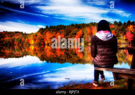 Una bella donna cinese guardando la caduta delle foglie che riflette in acqua mentre è seduto su un tavolo da picnic in autunno a Burr Pond State Park a tor Foto Stock