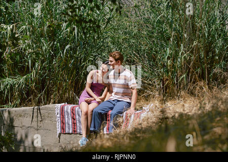 Coppia giovane seduto sul muro nel parco, Los Angeles, California, Stati Uniti d'America Foto Stock