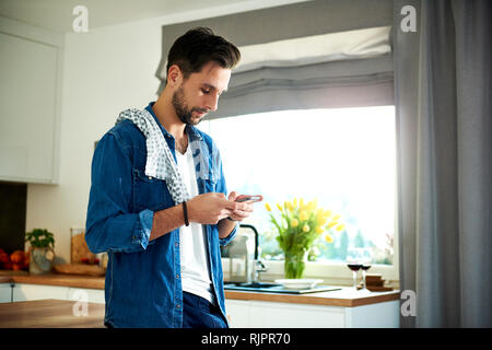 L'uomo utilizza lo smartphone in cucina Foto Stock