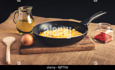 Close up foto di uova strapazzate con Paprica macinata, cipolle, olio e il mestolo di legno - stile rurale. Il giallo delle uova strapazzate in padella nera sulla tavola di legno. Foto Stock