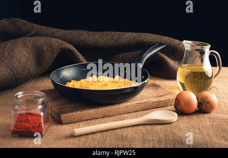 Close up foto di uova strapazzate con Paprica macinata, cipolle, olio e il mestolo di legno - stile rurale. Il giallo delle uova strapazzate in padella nera sulla tavola di legno. Foto Stock