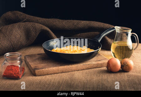 Close up foto di uova strapazzate con Paprica macinata, cipolle e olio - stile rurale. Il giallo delle uova strapazzate in padella nera sulla tavola di legno. Foto Stock