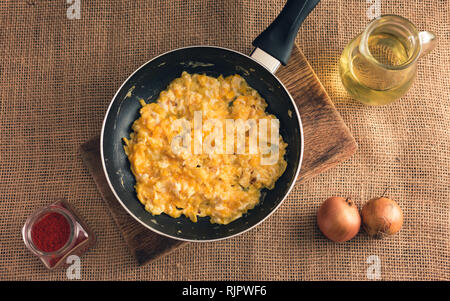 Foto di uova strapazzate con Paprica macinata, cipolle e olio di cui sopra - stile rurale. Il giallo delle uova strapazzate in padella nera su sfondo di iuta. Foto Stock