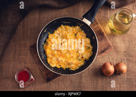 Foto di uova strapazzate con Paprica macinata, cipolle e olio di cui sopra - stile rurale. Il giallo delle uova strapazzate in padella nera su sfondo di iuta. Foto Stock