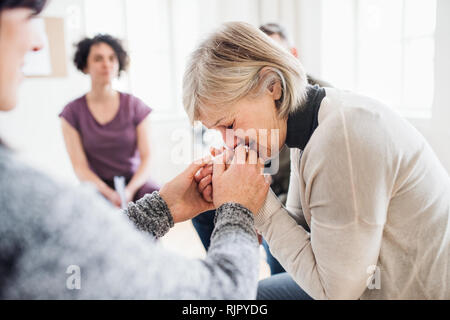 Un senior premuto donna che piange durante la terapia di gruppo. Foto Stock