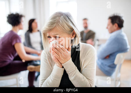 Un ritratto di senior premuto donna che piange durante la terapia di gruppo. Foto Stock