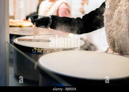 Realizzazione di Crepes Pancake in open festa del mercato equo. Una mano è rendere crepes all'aperto su una griglia metallica con bastone di legno su un outdoor summer fest Foto Stock