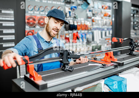 Bello operaio in uniforme scegliendo professional tagliapiastrelle nella costruzione shop Foto Stock