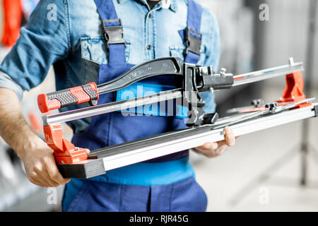 Bello operaio in uniforme scegliendo professional tagliapiastrelle nella costruzione shop, vista da vicino Foto Stock