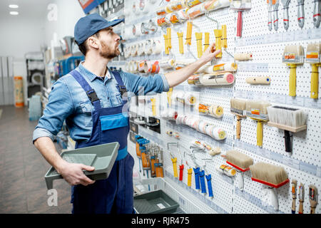 Bello operaio in uniforme scegliendo Strumenti per la pittura a l'edificio shop Foto Stock