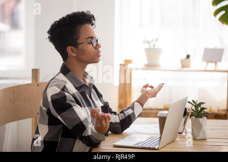 Calma donna africana prendendo break fare yoga a scrivania da ufficio Foto Stock