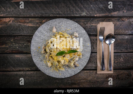 La pasta italiana Le fettuccine con formaggio, pollo e funghi, servita sulla splendida piastra in ceramica con le posate. Foto Stock