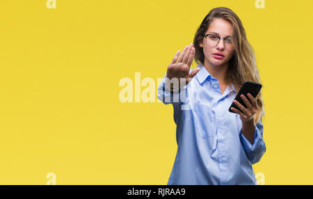 Giovane bella bionda business donna utilizza lo smartphone su sfondo isolato con mano aperta facendo segno di stop con gravi e fiducioso di espressione, Foto Stock