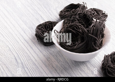 Pasta di colore nero in una piastra bianca su un tavolo bianco sullo sfondo. Il concetto è non semplici piatti. Realizzato da frumento duro con il nero di seppia Foto Stock