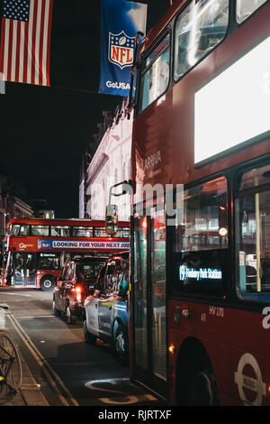 London, Regno Unito - 17 dicembre 2018: Nero i taxi e gli autobus su Regent Street, Londra, di notte. La strada è decorata con bandiere di NFL per celebrare le anche Foto Stock