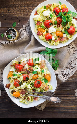 Fettuccine con pomodori al forno, pancetta e formaggio mozzarella su legno rustico sfondo. Vista dall'alto. Foto Stock