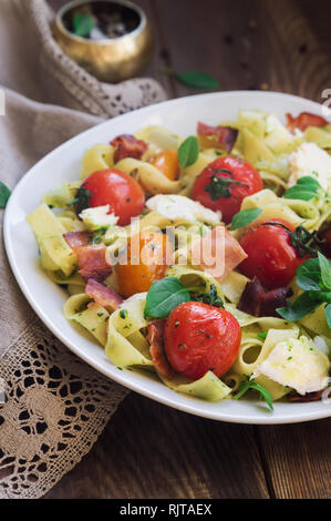 Fettuccine con pomodori al forno, pancetta e formaggio mozzarella su legno rustico sfondo. Messa a fuoco selettiva. Foto Stock