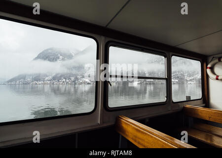 Vista sulla città di Hallstatt e Alpi dall'interno del passeggero traghetto sul lago. I posti vuoti in primo piano. Foto Stock