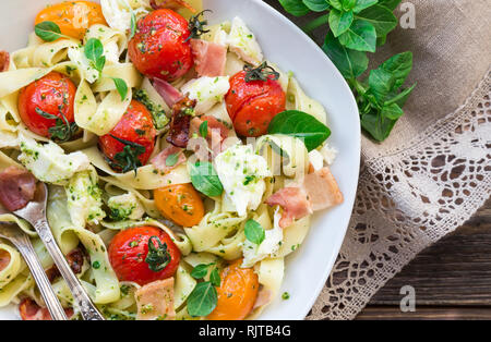 Fettuccine con pomodori al forno, pancetta e formaggio mozzarella su legno rustico sfondo. Vista dall'alto. Foto Stock