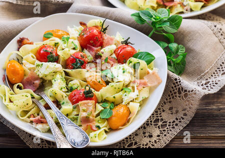 Fettuccine con pomodori al forno, pancetta e formaggio mozzarella su legno rustico sfondo. Messa a fuoco selettiva. Foto Stock