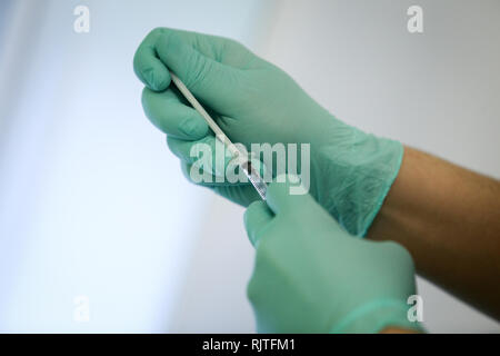 Dettagli con le mani di un medico, gomma da indossare i guanti chirurgici e di estrazione di sangue e di plasma da una fiala con una siringa Foto Stock