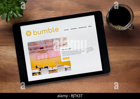 Il sito di dating Bumble app è visto su un tablet iPad, su di un tavolo di legno lungo con un caffè espresso e una pianta di casa (solo uso editoriale). Foto Stock