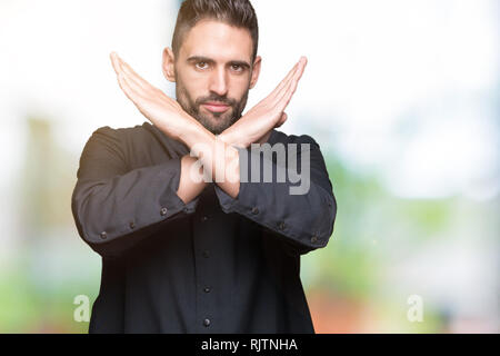 Giovane sacerdote cristiano su sfondo isolato rifiuto espressione bracci di incrocio facendo segno negativo, volto arrabbiato Foto Stock