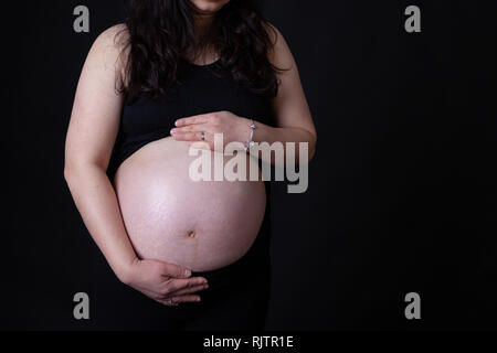 Giovani asiatici madre incinta con mani tenendo il suo bambino nella pancia con copia spazio. Isolato su sfondo nero. Foto Stock