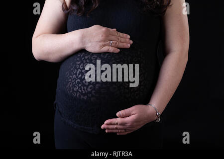 Giovani asiatici madre incinta con mani tenendo il suo bambino nella pancia con copia spazio. Isolato su sfondo nero. Foto Stock