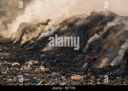 Un giovane bambino la raccolta di materiali riciclabili tra fumo tossico da discarica a Rishikesh, Uttarakhand, India Foto Stock