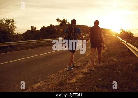 I viaggiatori con zaini vai su strada al tramonto. Foto Stock