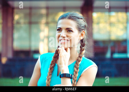 Eccitato atletica giovane donna abbigliamento sportivo in piedi con asciugamani su collo e sorridente sul background urbano Foto Stock