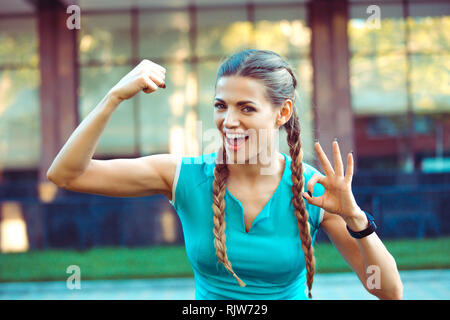 Donna sorridente che mostra bicipite Foto Stock