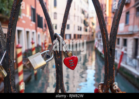 Combinazione di colore rosso a forma di cuore e altri lucchetti sul ponte a Venezia, Italia. Giornata di sole, edifici storici e il canale in background. Chiudere Foto Stock