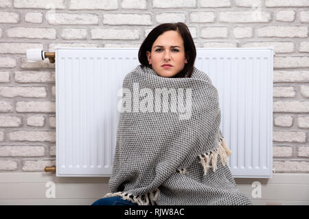 Giovane donna avvolta in una coperta seduti vicino al radiatore a casa Foto Stock