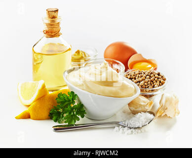 Ingredienti per rendere la maionese cremosa con limone fresco, tuorli, senape, olio, aglio e sale su uno sfondo bianco Foto Stock