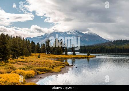 Il lago di riva del Lago Maligne, dietro di esso la gamma della montagna di Queen Elizabeth gamme, cielo nuvoloso, Jasper National Park, montagne rocciose Foto Stock