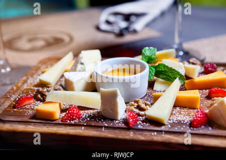 Il piatto di formaggi serviti con uva, miele e i dadi su uno sfondo di legno. Vari tipi di formaggio Foto Stock