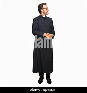 La mezza età sacerdote uomo indossare accappatoio cattolica sorridente guardando al lato con le braccia incrociate convinto e fiducioso Foto Stock