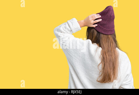 Giovane bella bruna hipster donna che indossa occhiali e cappello invernale su sfondo isolato indietro pensando di dubbio con la mano sulla testa Foto Stock