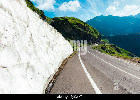 Parete di neve dalla strada in montagna. avvolgimento in salita a serpentina lungo le colline erbose. splendida primavera meteo. bella cloudscape sopra il Foto Stock