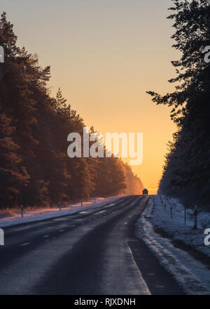 Silhouette di una vettura sulla strada asfaltata in nevoso inverno la luce del tramonto. New Scenic 5 posti di abeti con la neve fredda sui rami da strada Foto Stock